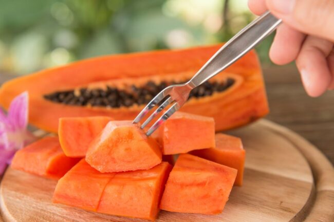 person sticking a dessert fork into a piece of diced papaya - the high vitamin c content makes it good for varicose veins